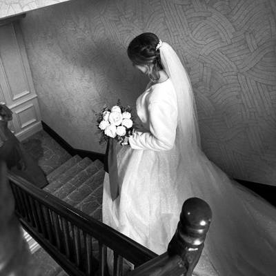 The bride descends a staircase holding a bouquet of white flowers, black and white.