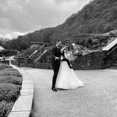 The couple dance on a stone terrace with wooded hills behind them, black and white.