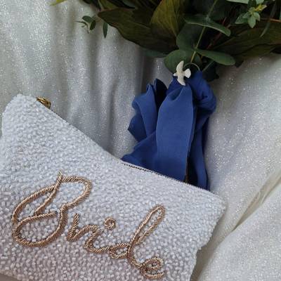 A beaded clutch reading Bride next to a bouquet tied with a blue ribbon.